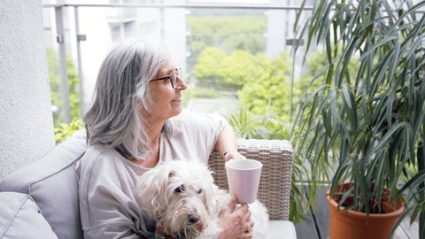 Senior woman with coffee and dog at home, resting outdoors on balcony.