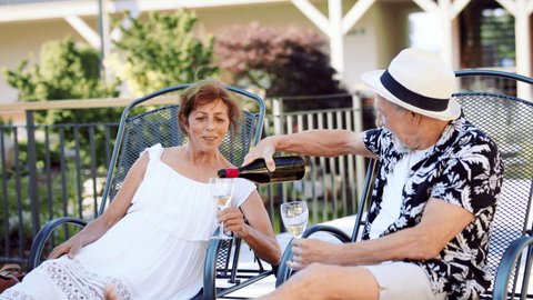 Senior couple on sunbeds outdoors on holiday, drinking wine.
