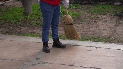 closeup of a girl with gloves cleaning the street with a straw broom with wooden magician