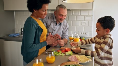 Smiling mixed race family with they son standing in the kitchen preparing sandwich for breakfast at home.