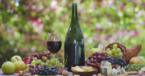 Still life with wine, different grapes and autumn fruits, cheeses against the background of autumn foliage with beautiful bokeh. 