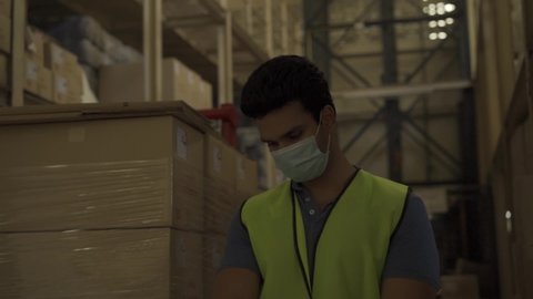 Young Indian factory warehouse worker wearing face mask getting body temperature check with infrared thermometer before working. Security measure at workplace in Coronavirus pandemic - HD Slow Motion