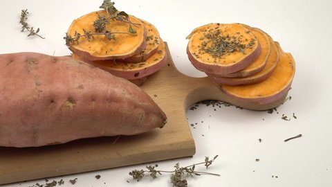 Tuber and slices of fresh sweet potato, dry thyme lie on a wooden board on a white background
