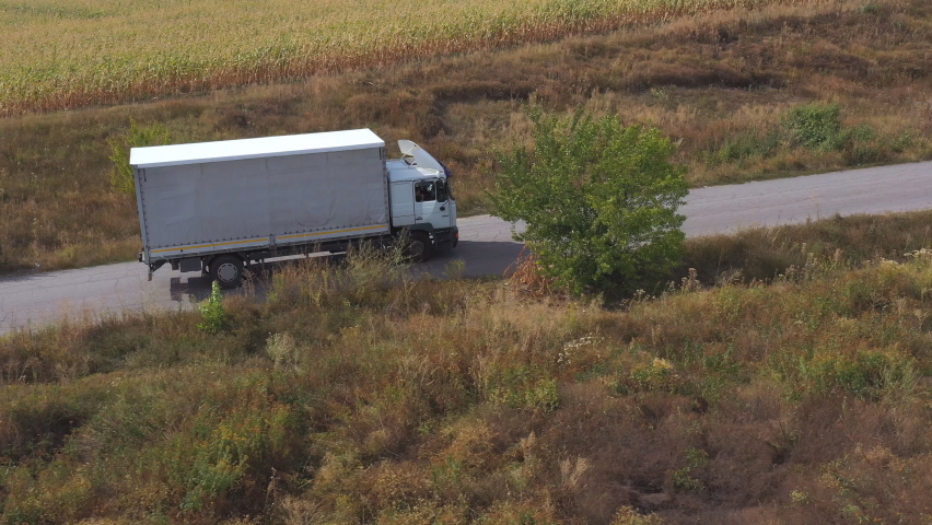 Aerial shot of truck with cargo trailer driving on road and transporting goods. Flying over delivery lorry moving along highway passing near fields in countryside. Scenic nature scene. Side view Royalty-Free Stock Footage #1060114553