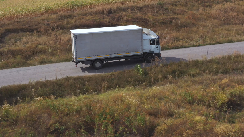 Aerial shot of truck with cargo trailer driving on road and transporting goods. Flying over delivery lorry moving along highway passing near fields in countryside. Scenic nature scene. Side view Royalty-Free Stock Footage #1060114553