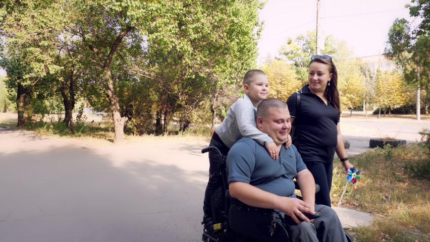 Wheelchair man. Handicapped man. young disabled man in an automated wheelchair walks with his family, wife and small child, along city alley on sunny autumn day. | Shutterstock HD Video #1060116458
