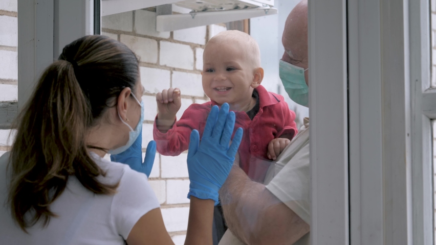Mother in medical mask communicated with baby with father through glass window on door. Covid-19 pandemic sick people in quarantine. Meetings with family. Mother child relationship. Social distance | Shutterstock HD Video #1060117835