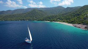 Aerial drone video of beautiful sail boat sailing near paradise turquoise sandy beach of Milia covered in pine trees, Skopelos island, Sporades, Greece