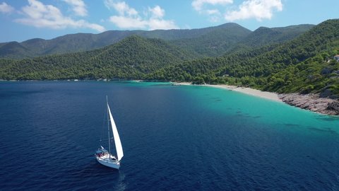 Aerial drone video of beautiful sail boat sailing near paradise turquoise sandy beach of Milia covered in pine trees, Skopelos island, Sporades, Greece