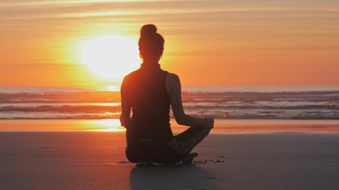 Silhouette of a slim woman on the beach at a beautiful sunset, Practice of yoga breathing techniques.