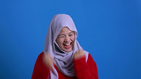 Beautiful Asian muslim woman wearing hijab shows winning victory gesture, excited happy to see something good