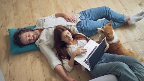 A Lovely Couple Lying on the Floor Using a Laptop, spouses enjoying of Each Other. Near a Couple Lying A Cute Dog. Happy Young Married Couple Talking.