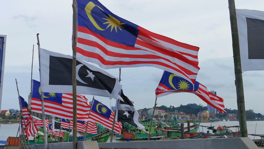 Static view of Malaysian and Terengganu state flags fluttering on a windy day against traditional wooden fishing boat docking at a jetty in Kuala Terengganu, Malaysia. Royalty-Free Stock Footage #1060128845