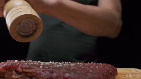 Professional chef peppers meat fillet steak from hand pepper mill, close up slow motion.
