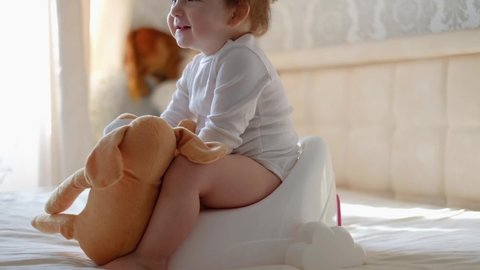Baby legs hanging from a pot. The boy is sitting on the potty. Funny baby sitting on the morning pot in the bedroom