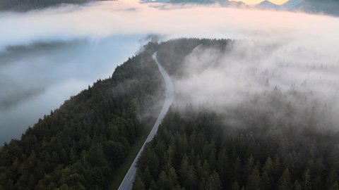 Aerial view descending over a mountain road covered by fog at sunrise