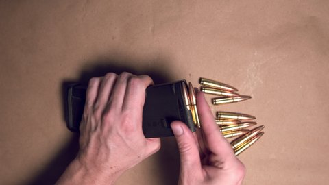 Close up shot of hands loading a rifle magazine with bullets. Top down shot