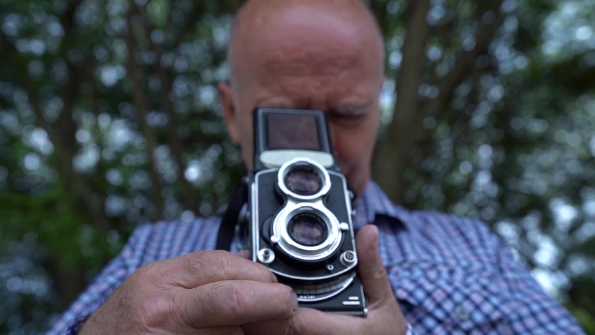 Grandpa is holding an unusual camera. An elderly man in a shirt on the street. The concept of a photographer in nature in a Park with a background of trees.