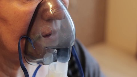 Extreme close up shot of an older woman using a respiratory mask inhaling medicine to clear out her throat and sinuses.