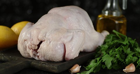Raw the whole chicken on the cutting board rotates. On a black background.
