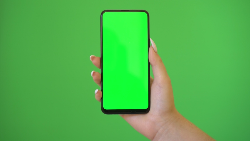 Woman hand holds a smartphone with greeen screen over a green background. | Shutterstock HD Video #1060137965