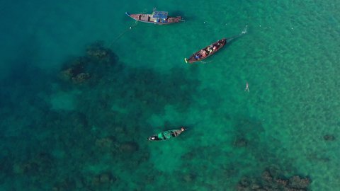 View from above, stunning aerial view of some longtail boats and tourists snorkeling in a beautiful, turquoise sea. Phi Phi Island, Thailand.