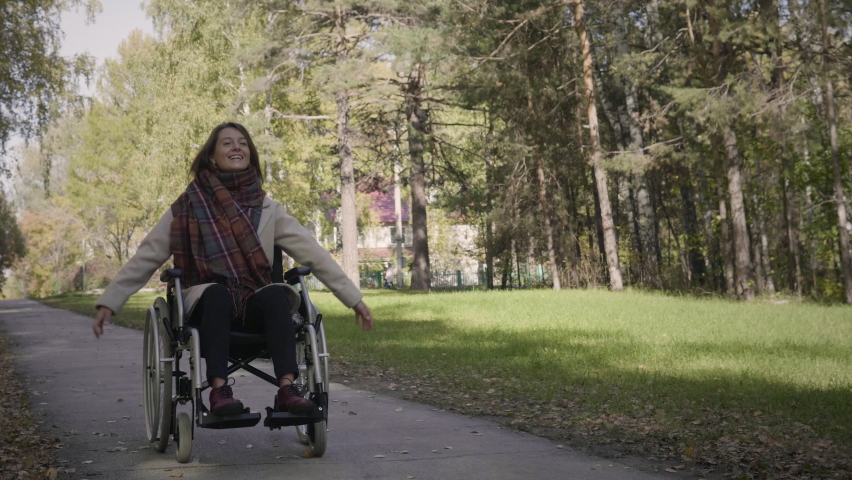 Happy cheerful disabled woman in the wheelchair enjoying the walk in the beautiful autumn forest. Woman is laughing and feels exciting | Shutterstock HD Video #1060138724
