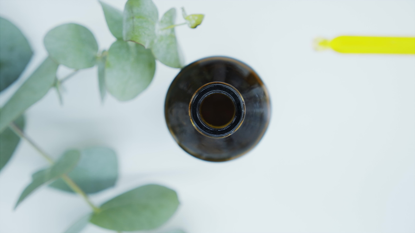 Close-up of a pipette with oil and the neck of a dark bottle with a branch of eucalyptus. Eucalyptus extract, aromatic oil. Natural cosmetics for hair and skin care. Top view. | Shutterstock HD Video #1060139309