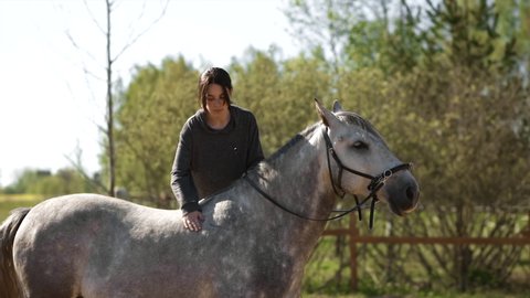 Female equestrian with long hair mounts grey horse during training