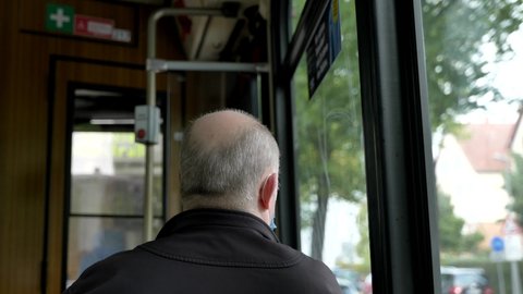 Interior and selected focus view at the back of old male passenger with face protection mask who sit in light rail tram or train in Germany during epidemic of COVID-19 virus with new normal concept.