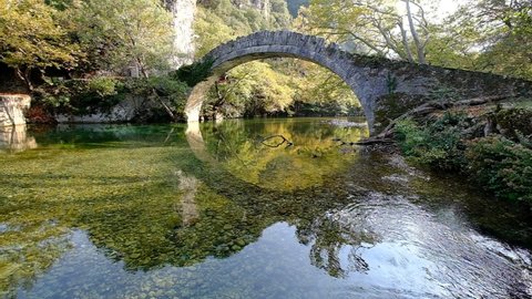 An Ottoman bridge above the peaceful Voidomatis river, in a fantastic morning backlight, slow motion video, Klidonia Bridge, Greece.