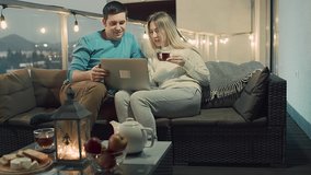 Couple celebrating, talking on video call on laptop, drinking tea, spend free time on terrace in home. Online chat with Family, long distance communication. Holidays time. 4K video Slow motion.