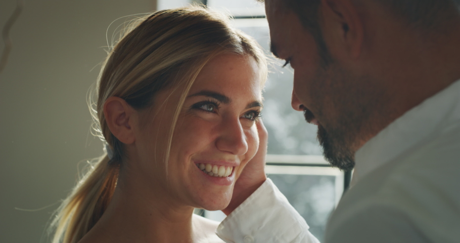 Authentic shot of young happy smiling married couple is enjoying time together is hugging as sign of timeless love in a kitchen at home. | Shutterstock HD Video #1060148315
