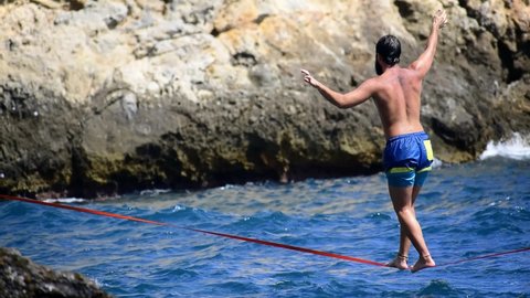 Slacklining sport. Sportsman keeps balance over a slack line. Slackline sport over water. Practice of slack line at mediterranean sea.