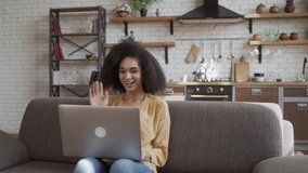 Happy african american young woman looking at computer screen, waving hello. Pleasant attractive mixed race female holding video call at home on the couch