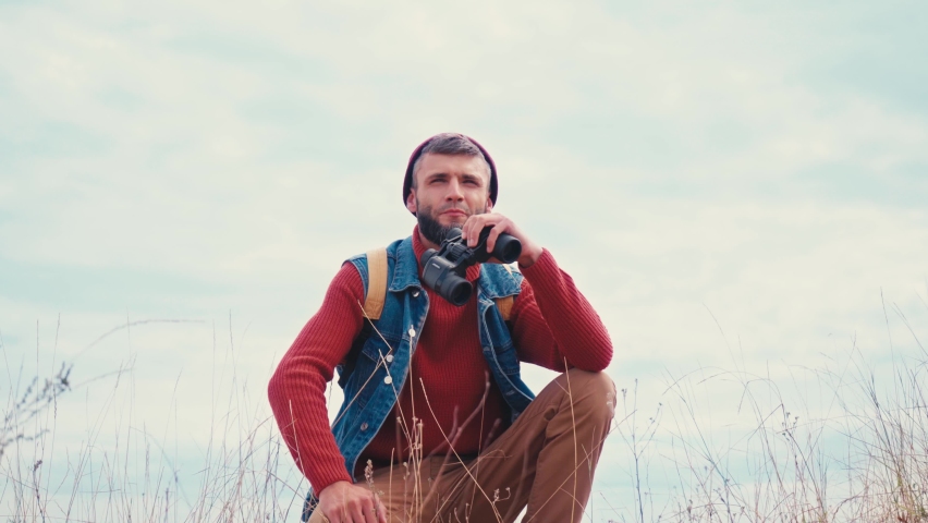 Low angle view of tourist sitting and looking through binoculars on grass