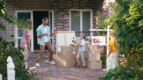 mother throwing football to kids near husband, carton boxes and new house