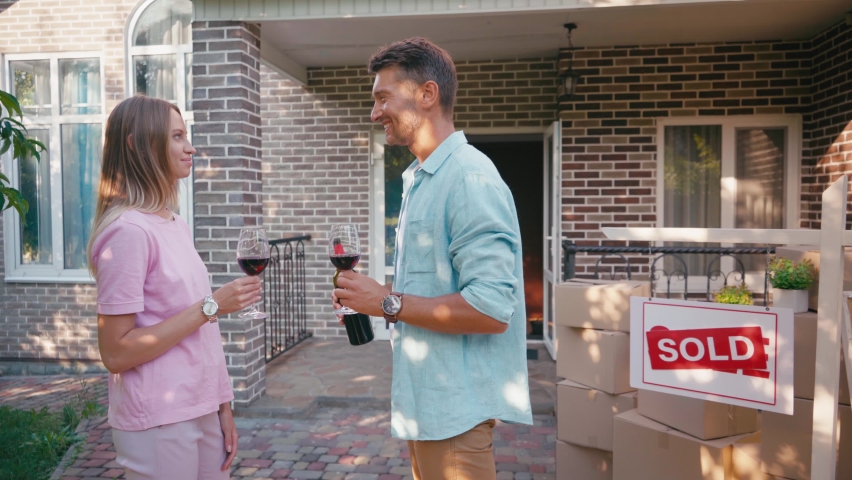 man holding bottle of wine while clinking glasses with wife near new house