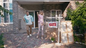 joyful couple jumping and dancing near boxes and new house