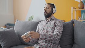 Slow motion of carefree Middle Eastern man playing with smartphone enjoying gaming application wearing headphones. People and fun concept.