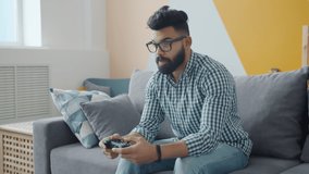 Slow motion of young mixed race man enjoying video game relaxing on couch in cozy apartment playing alone. People, housing and hobby concept.