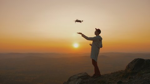 A man standing on top of the mountain and starts drone from his hand, aircraft takes off into the sky at sunset. guy starts drone against backdrop of foggy picturesque view to take pictures of nature.