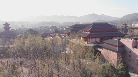 Aerial flight above the castle with walls. Bright trees with sun reflection in old Chinese town. Traditional temple. Mountains in China. Popular travel destination in Asia. 