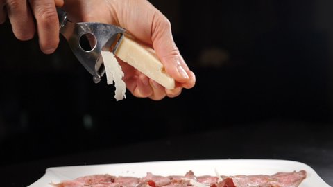 Grating parmesan cheese with grater in kitchen. Cooking food in restaurant. Traditional Italian cuisine. Parmesan Shavings falling on roast beef in slow motion. Full hd