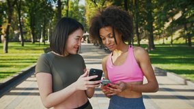 Modern generation communication. Outdoor portrait of asian and african american female friends looking at smartphone and laughing, discussing social media in park