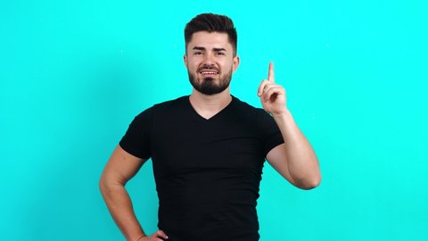 Young bearded Caucasian man in a black T-shirt looks around, thinks, looks left and right, and at the end an idea comes to him. Isolated in the studio on a blue background.