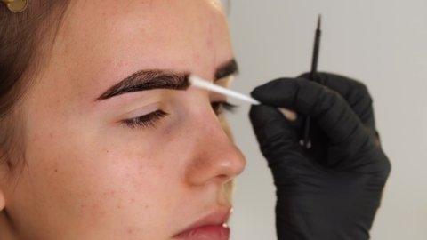 Eyebrow coloring. Professional styling, correction and lamination procedures of female eyebrows in beauty salon. Closeup view of client face and stylist's hands working in black gloves.