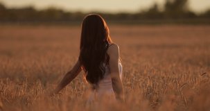 Beautiful young woman enjoys life walking on a wheat field at sunset in summer