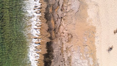 Aerial overhead drone clip over a beach with waves crushing the rocks on the shore in Kavala, Macedonia, Greece