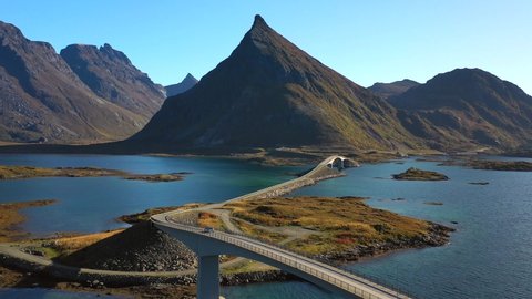 Drone shot of a car driving over a bridge in the Lofoten islands, mountains in the background, sunny, autumn day, in Nordland, North Norway - dolly, aerial view
